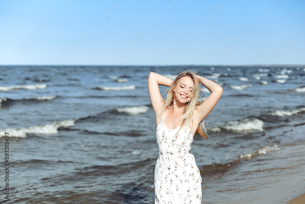 Happy blonde beautiful woman on the ocean beach standing in a white summer dress, raising hands Happy blonde beautiful woman on the ocean beach standing in a white summer dress, raising hands