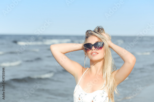 Happy blonde woman in free happiness bliss on ocean beach standing with sun glasses and posing