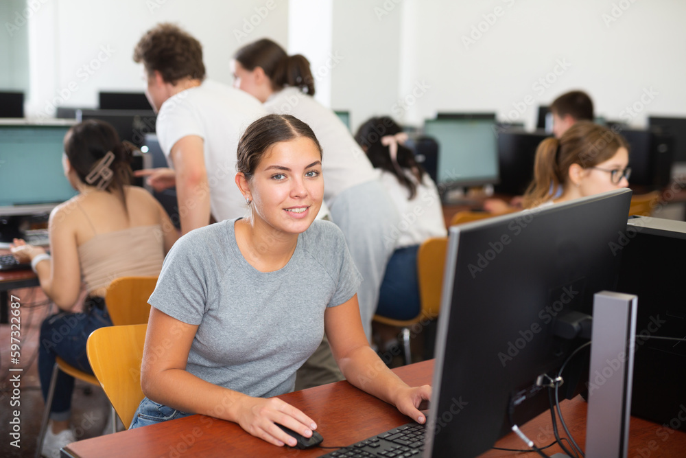 Fototapeta premium Smiling female student using PC and studying computer science in the classroom