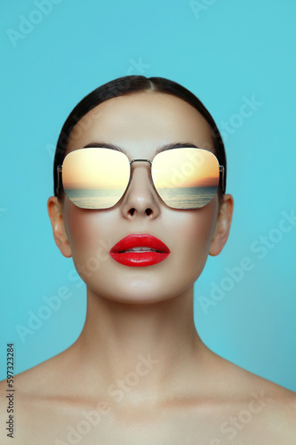 Attractive woman in stylish sunglasses on light blue background. Sea sunset reflecting in lenses