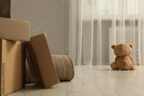 Cute lonely teddy bear on floor near boxes indoors, back view