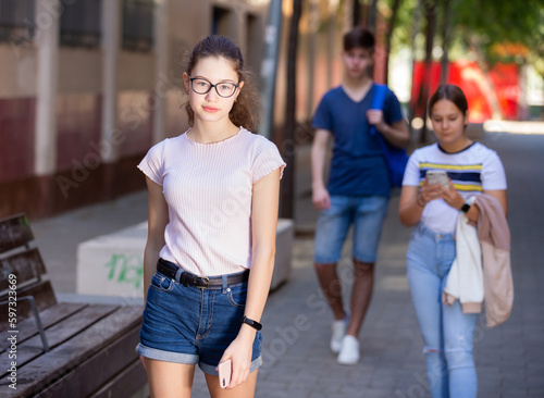 Cute smiling teenage girl in glasses enjoying walk around city in warm summer day