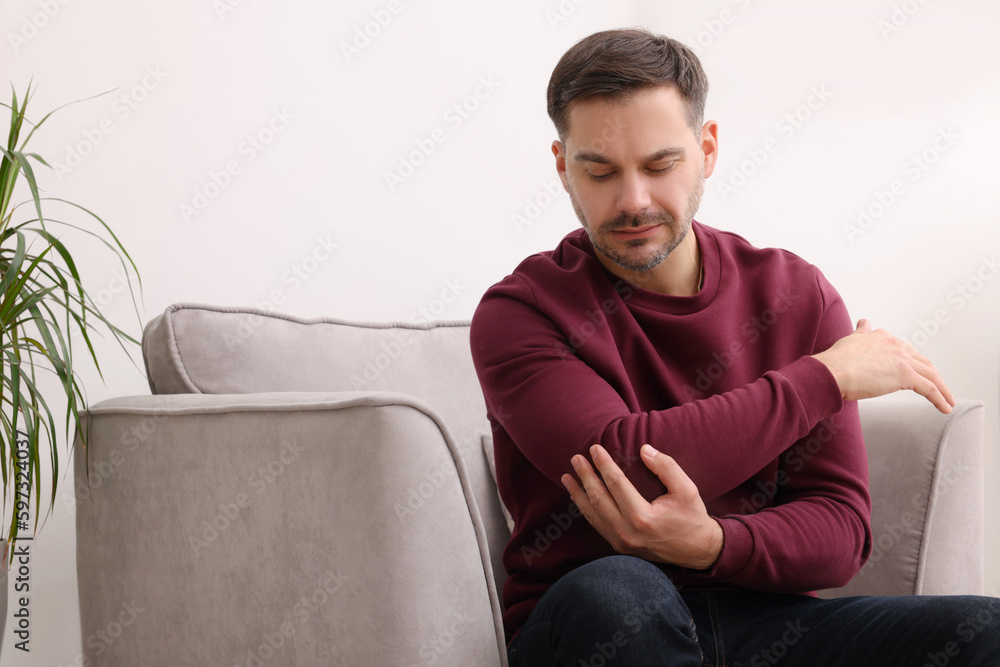 Man suffering from pain in his elbow on armchair indoors Man suffering from pain in his elbow on armchair indoors