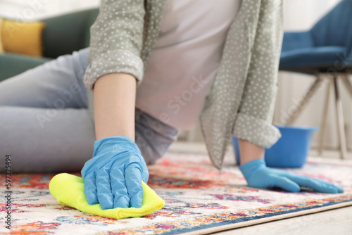 Woman in rubber gloves cleaning carpet with rag indoors, closeup. Space for text