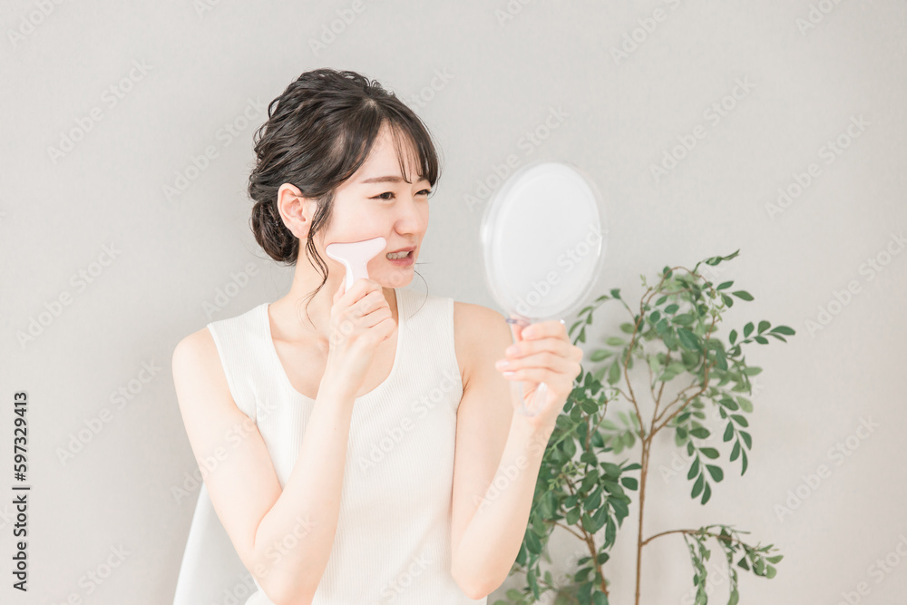 鏡を見ながらかっさでフェイスマッサージをして痛がるアジア人女性

