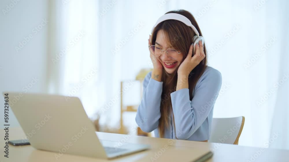 Happy young asian woman relaxing at home. Smiley female working on computer laptop. Girl using video call to friend, Wearing headset listening to music Happy young asian woman relaxing at home. Smiley female working on computer laptop. Girl using video call to friend, Wearing headset listening to music