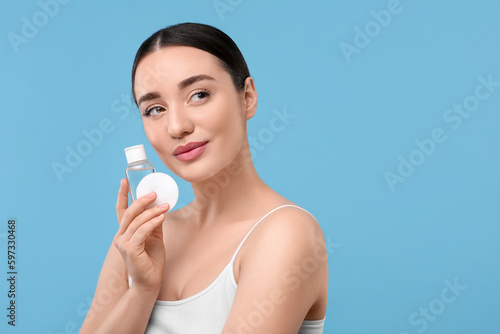 Beautiful woman with makeup remover and cotton pad on light blue background, space for text