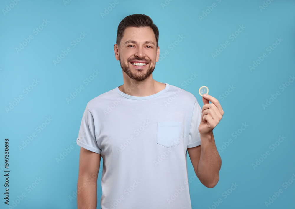Happy man holding condom on light blue background Happy man holding condom on light blue background