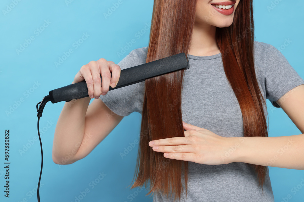 Woman using hair iron on light blue background, closeup Woman using hair iron on light blue background, closeup