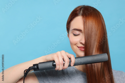 Beautiful woman using hair iron on light blue background, space for text