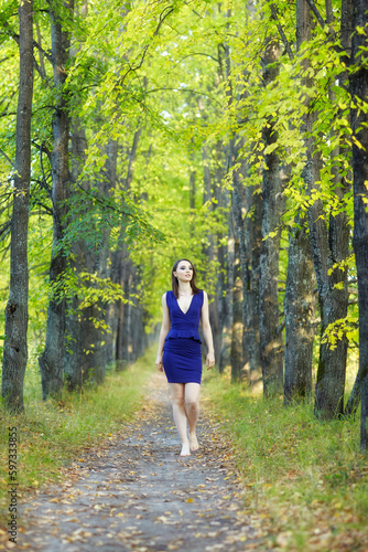Female in blue dress walking along autumn linden tree alley.