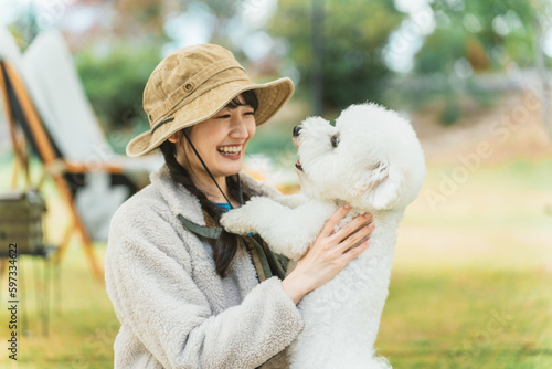 Photographie 秋冬のキャンプ場で愛犬を抱くキャンパーのアジア人女性（ビジョンフリーゼ）
