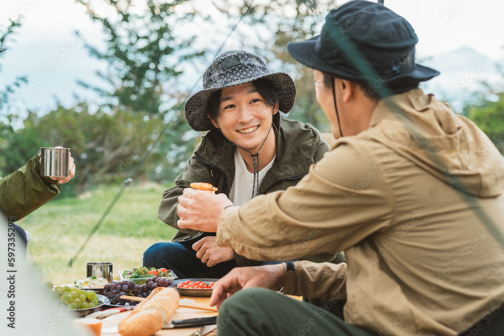 キャンプ飯を仲間と食べるアジア人男性キャンパー

