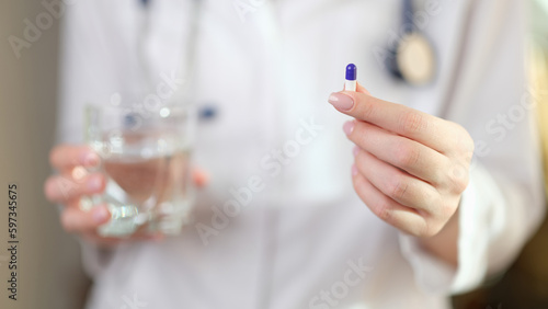 Female doctor holds vitamin pill and glass of water in hands