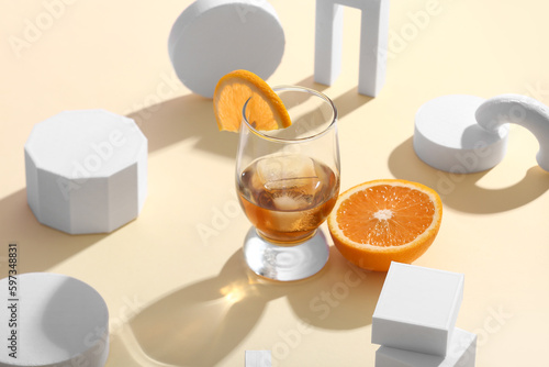 Glass of rum with orange slices, ice cubes and plaster figures on beige background