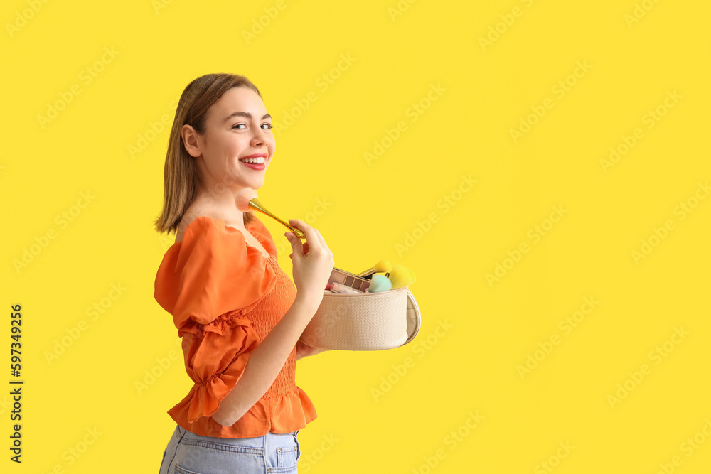 Young woman with cosmetic bag and makeup brush on yellow background Young woman with cosmetic bag and makeup brush on yellow background