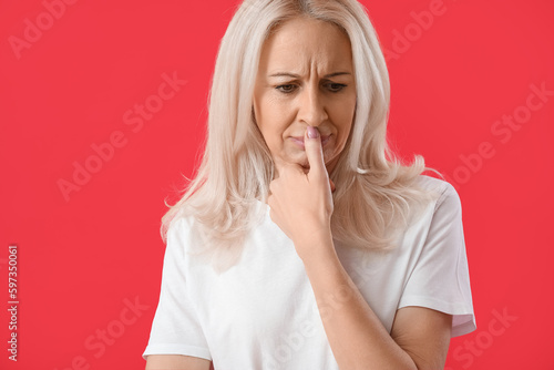 Thoughtful mature woman on red background, closeup
