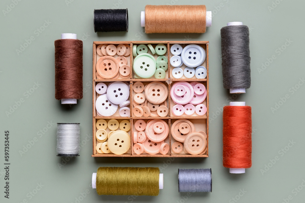 Composition with box of different buttons and thread spools on grey background Composition with box of different buttons and thread spools on grey background