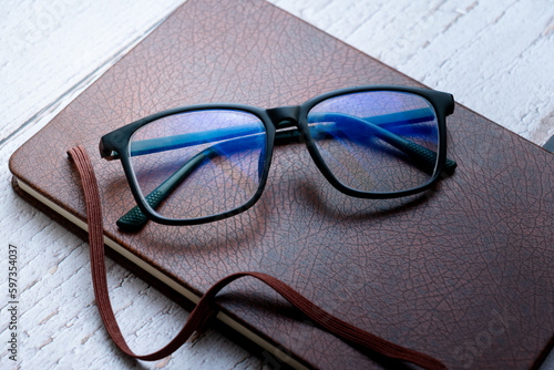 black frame blue light blocking technology anti glare spectacles glasses on brown textured book wooden background