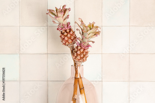 Vase with decorative pineapples near white tile wall, closeup