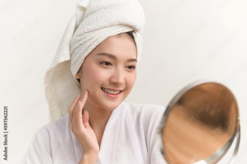 Close up portrait photo of young beautiful Asian woman taking care of her facial skin after apply face skin care cosmetic lotion moisturizer product and checking in mirror at home. Beauty care concept Close up portrait photo of young beautiful Asian woman taking care of her facial skin after apply face skin care cosmetic lotion moisturizer product and checking in mirror at home. Beauty care concept