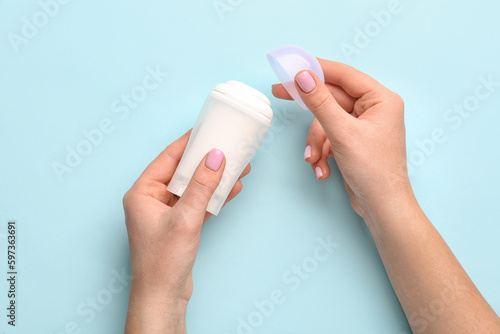 Female hands holding deodorant on blue background