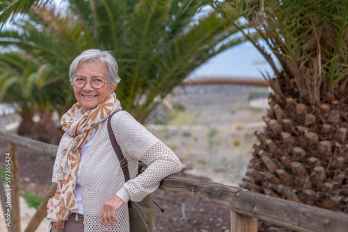 Portrait of senior gray haired woman with backpack in public park enjoying retirement, healthy lifestyle or vacation. Horizon over water. Copy space photo