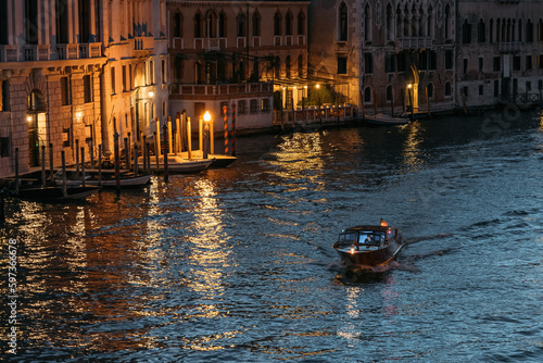 Lone motorboat floats the Grand Canal in Venice in glowing lights against the backdrop of blue water on a summer evening. Concept of romantic tourist trips in the ancient city of Italy. Copyspace