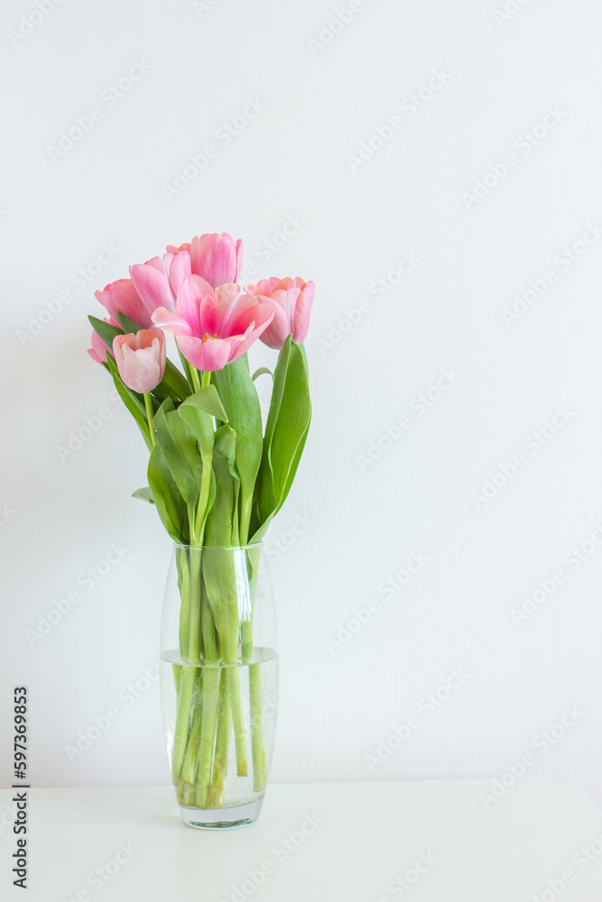 Pink tulips bouquet in glass vase on white background copy space