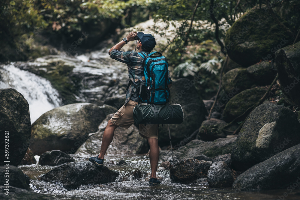 Hikers standing on the rock and use binocular to see animals and view landscape with backpacks and waterfall background in the forest. hiking and adventure concept.