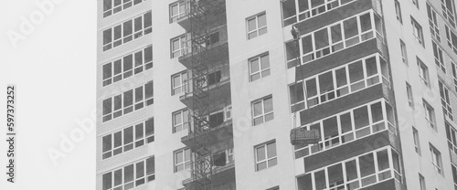 Monochrome concept of apartment building under construction close-up. Exterior of new multi-story residential building in grayscale. Background with walls, plastic windows and loggias. Copy space.