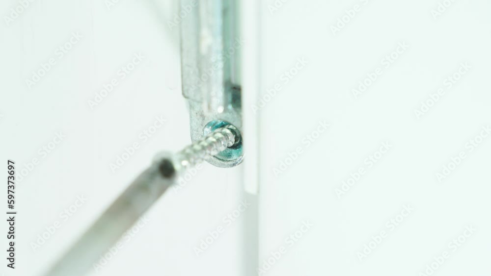 A Phillips screwdriver screws a metal part into the body of a plastic door, close-up A Phillips screwdriver screws a metal part into the body of a plastic door, close-up
