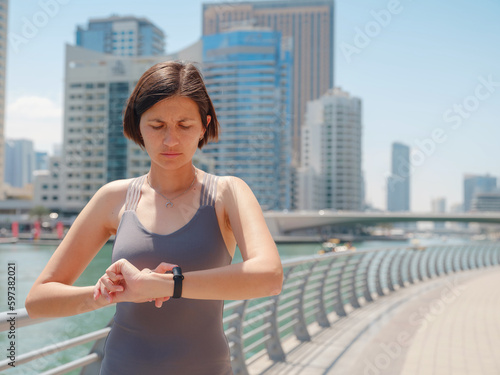 Young Asian female runner watch on heart rate monitor wrist watch band, smart wearable device, ready for running exercise in morning for healthy sport running in Dubai marina promenade