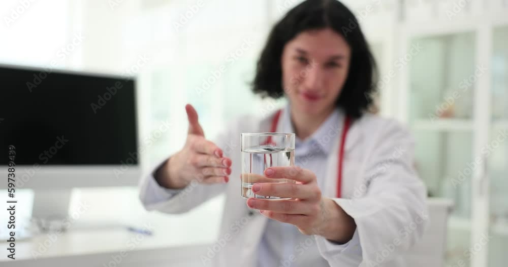 Careful male doctor offers glass of water to patient in clinic office. Young specialist takes care of sick person in hospital slow motion Careful male doctor offers glass of water to patient in clinic office. Young specialist takes care of sick person in hospital slow motion