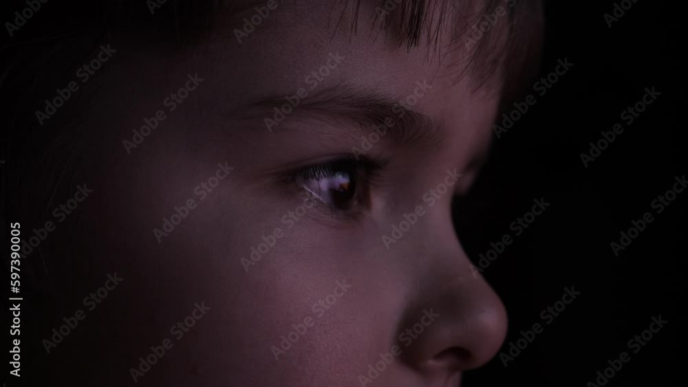 Close-up Face of Child Eyes While Person Using Tablet, Smartphone or Computer. Boy Watch Television at Evening. Video Game Entertainment Emotions Family. Portrait Little Kid While Watching TV. Close-up Face of Child Eyes While Person Using Tablet, Smartphone or Computer. Boy Watch Television at Evening. Video Game Entertainment Emotions Family. Portrait Little Kid While Watching TV.