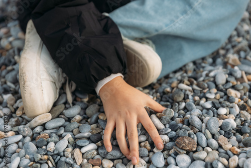 Fotografía Girl's hand touches stones, girl sit on pebble beach in cold weather