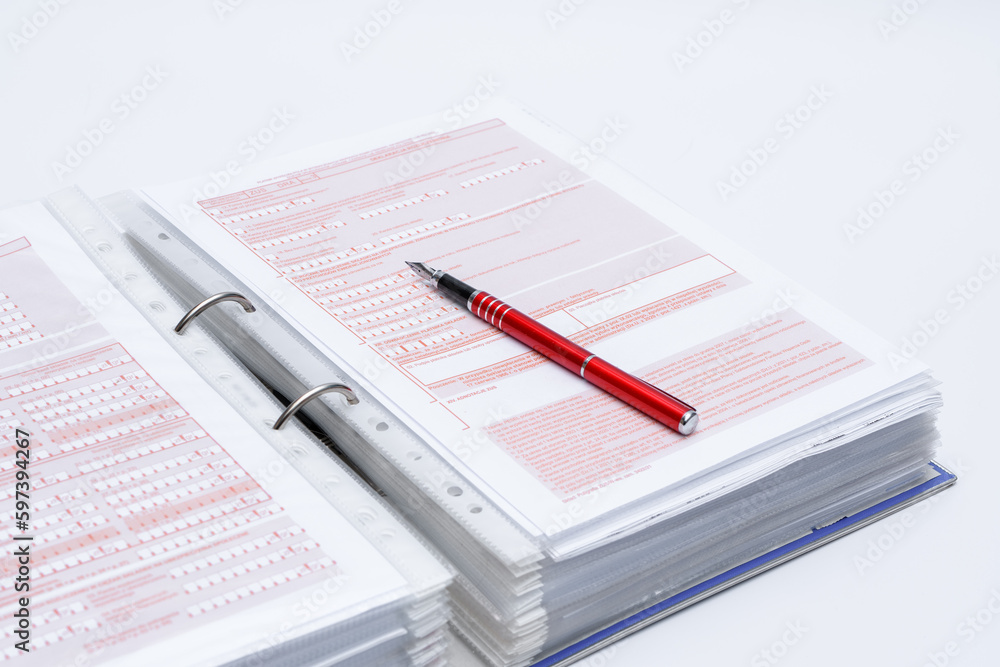 Segregator z dokumentami i leżący na nim czerwony długopis 