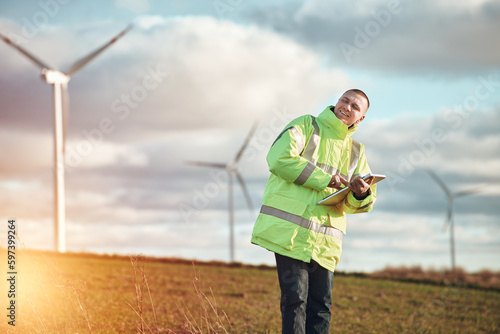 man working with tablet at a windmill farm generating electricity clean energy. man with a laptop with wind turbines background
