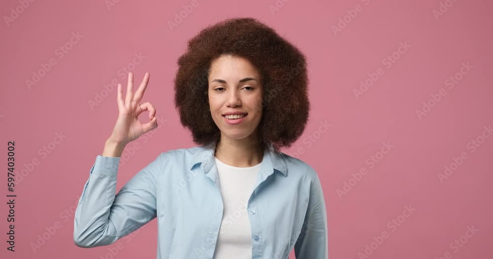 Cheerful young African American girl with afro hairstyle, noddle and showing OK sign hand gesture with fingers standing over pink studio background Cheerful young African American girl with afro hairstyle, noddle and showing OK sign hand gesture with fingers standing over pink studio background