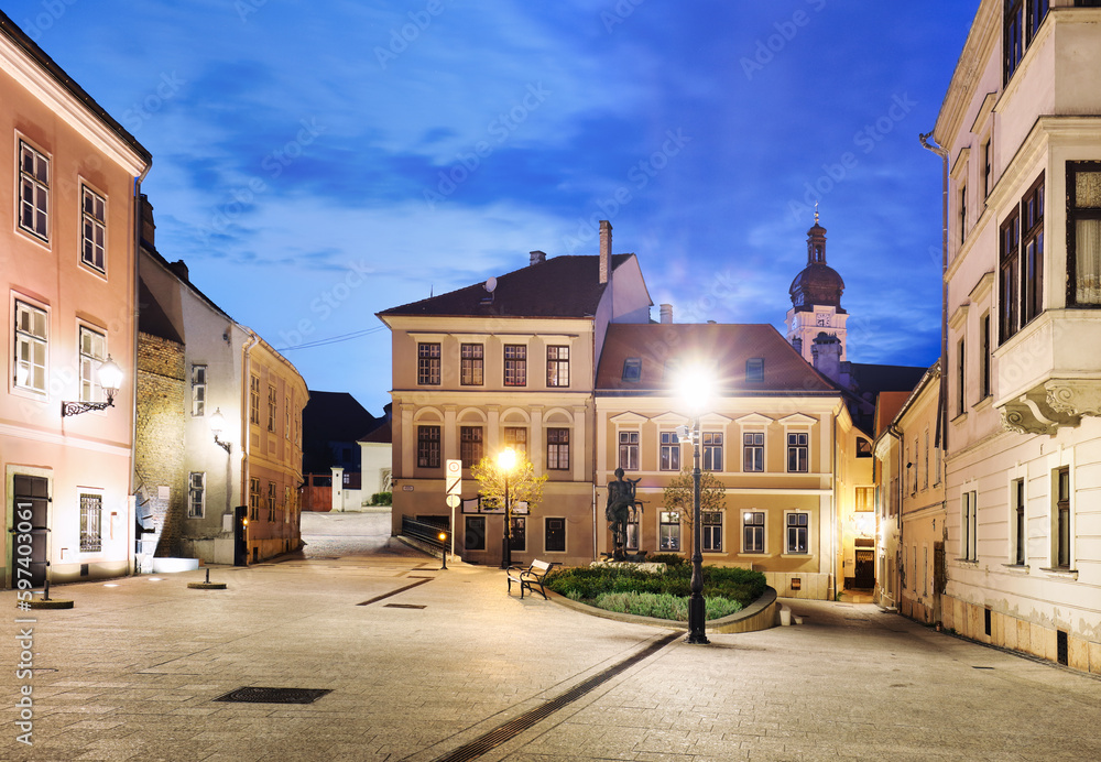 Hungary - Cozy little baroque square in the center of Gyor, with the bronze sculpture of Nimrod, in the background the Cathedral tower at night