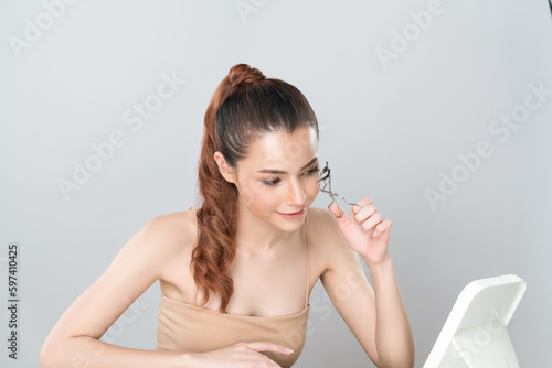Glamorous facial makeup, beautiful woman with perfect smooth cosmetic clean skin correct eyelash curler with metal mechanic beauty accessory in isolated background.