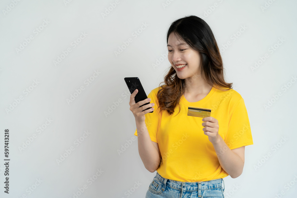 Naklejka premium Smiling asian woman paying with smartphone on internet, mobile phone and holding credit card standing on a white background