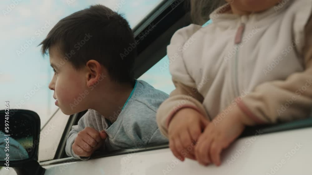 Adorable little brother and sister smiling while sticking their heads out the car window. Excited siblings waiting for their parents for a family trip. People Adorable little brother and sister smiling while sticking their heads out the car window. Excited siblings waiting for their parents for a family trip. People