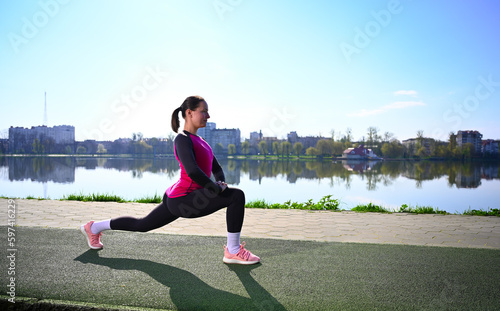 A young woman exercising at a tranquil lake during a beautiful morning. She's wearing workout clothes and appears focused and relaxed as she performs her exercise routine. Natural stunning backdrop.