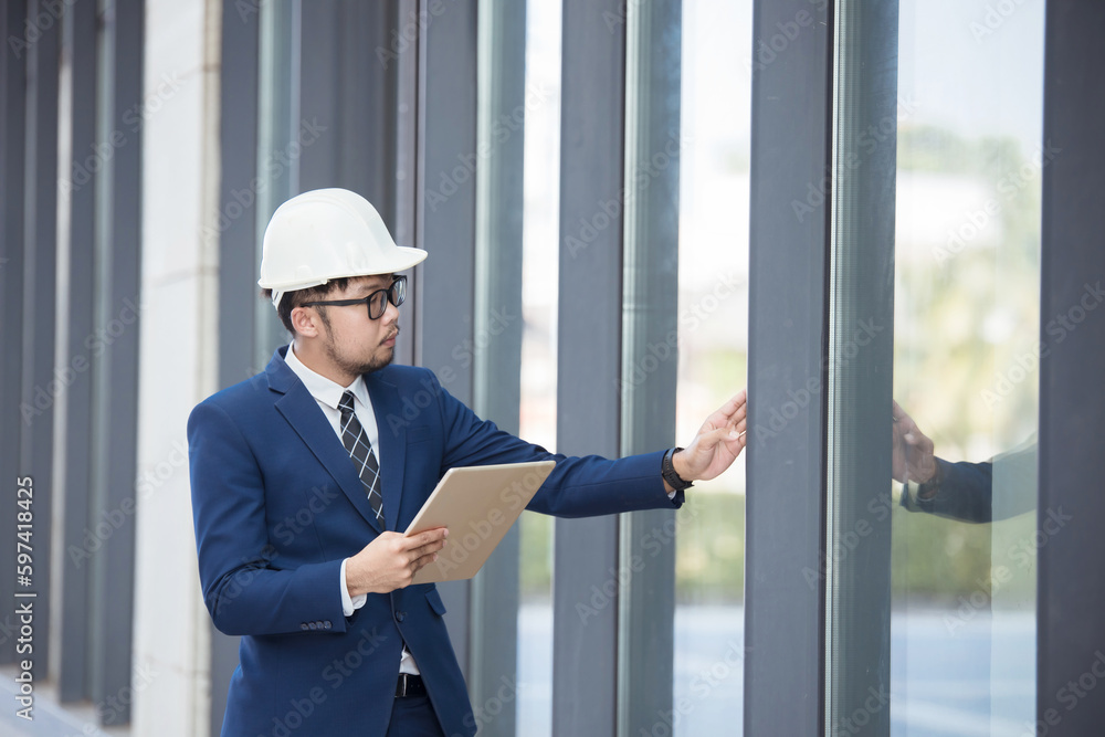 Handsome engineer wearing suit and hard hat or white helmet on building background. Engineer using tablet for checking construction about modern building. copy space for text. Handsome engineer wearing suit and hard hat or white helmet on building background. Engineer using tablet for checking construction about modern building. copy space for text.