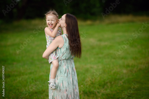 Happy mother holding her daughter in her arms, hugging,spending time together,enjoy happy family time. The concept of a happy family, family day, mother's day, countryside vacation, unity with nature.