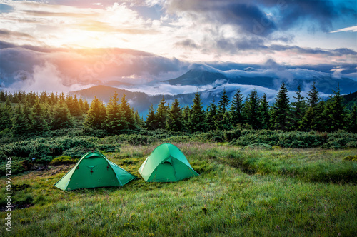 Two tourist tents in green mountains at sunset