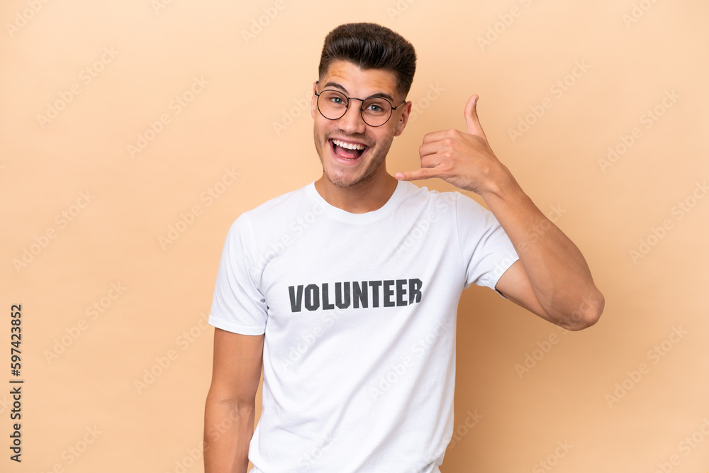 Young volunteer caucasian man isolated on beige background making phone gesture. Call me back sign Young volunteer caucasian man isolated on beige background making phone gesture. Call me back sign