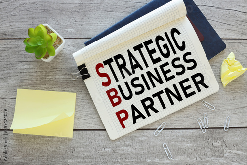 STRATEGIC BUSINESS PARTNER . clipboard on blue notepad near potted plant and yellow sticky notes. text on the page