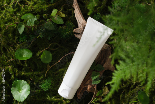 Scene for advertising cosmetic, promote branding with natural concept. White plastic tube container cleanser or moisturizer on forest background with moss, centella and other green leaves